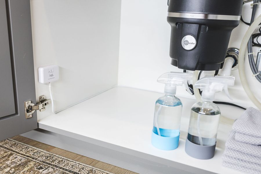 PuzL Detect installed inside a sink cabinet, cable routed around the drain and supply lines