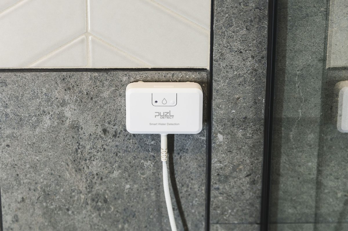 PuzL Detect unit mounted on a wall, front view, showing the alert LED and pairing button